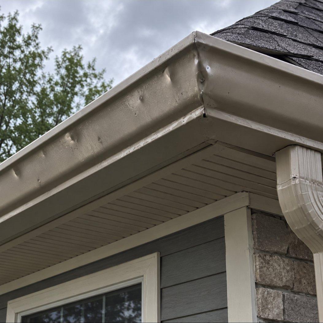 Beige gutter at the corner of a roof edge, dented in several spots by hail strikes