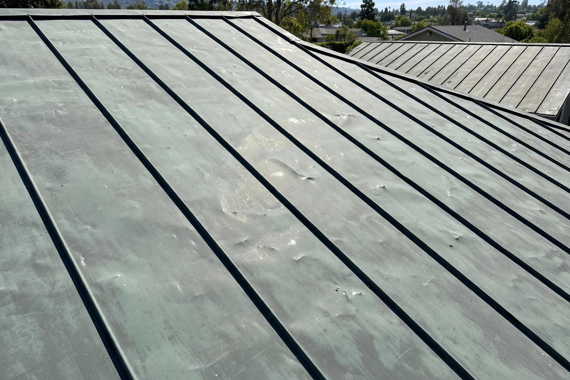 Standing-seam metal roof with small shallow dents scattered across the panels from hail